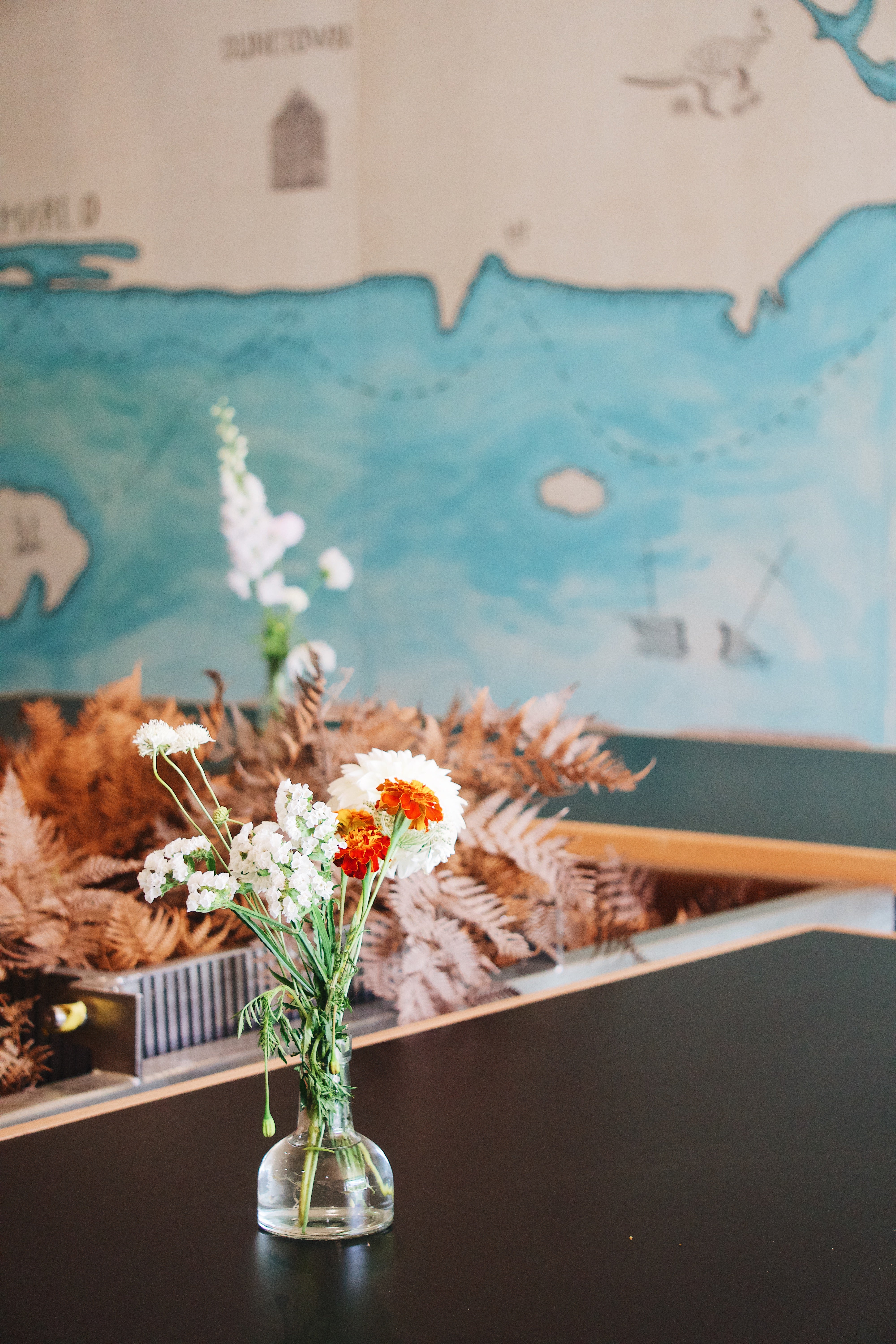 Vase with flowers on a table in front of a painted wall in Sailors Grave Brewing Barel Room